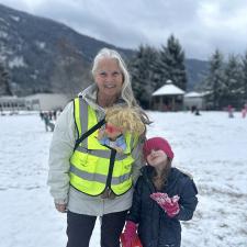 Woman wearing reflective vest poses with primary school student in schoolyard on a snowy day.