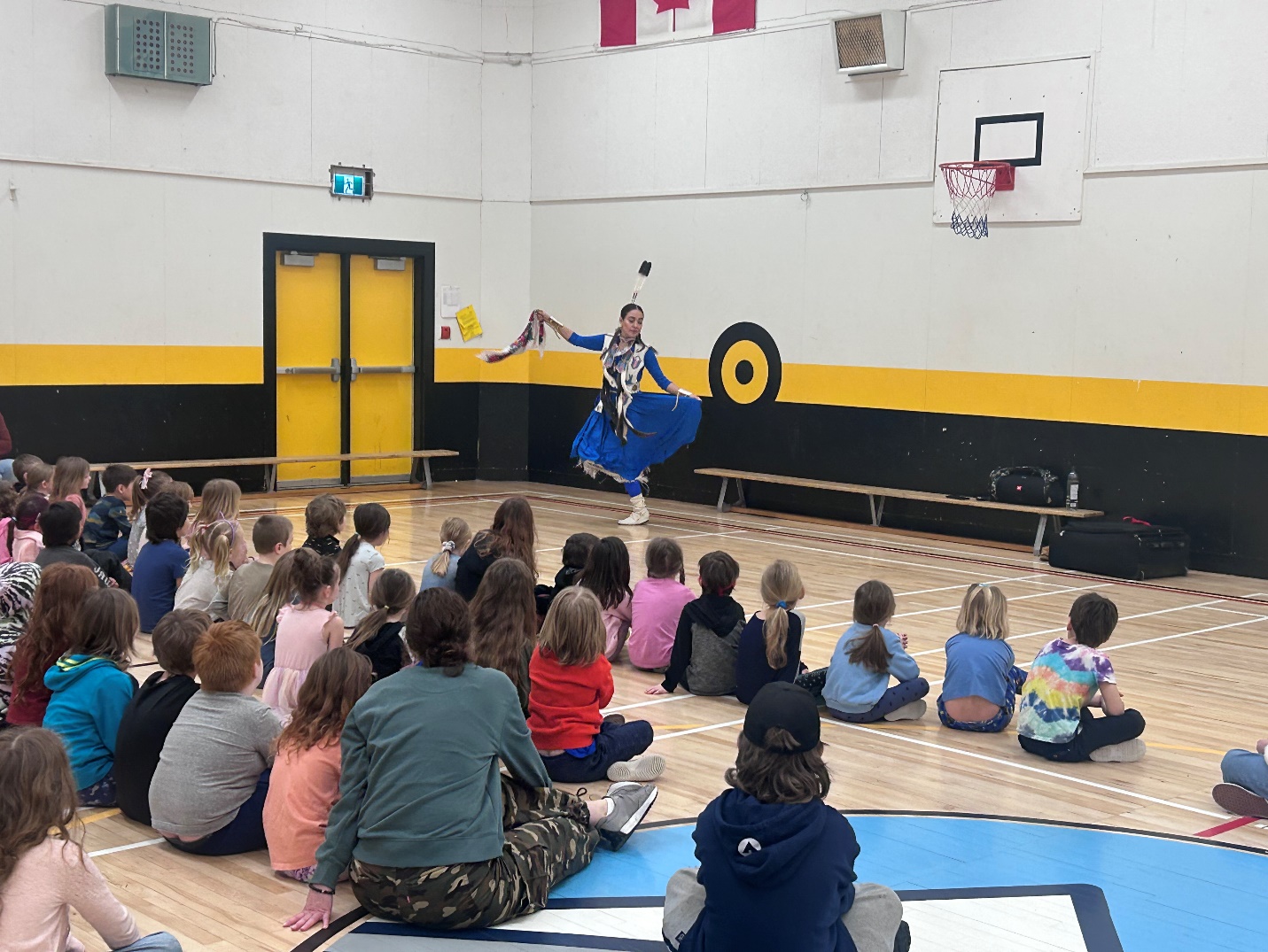 A group of kids sitting on the floor in a gym
Description automatically generated
