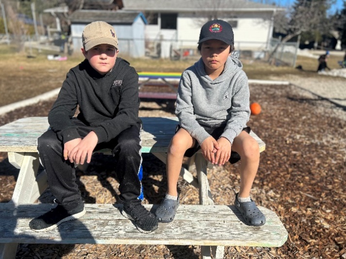 Two boys sitting on a picnic table
Description automatically generated