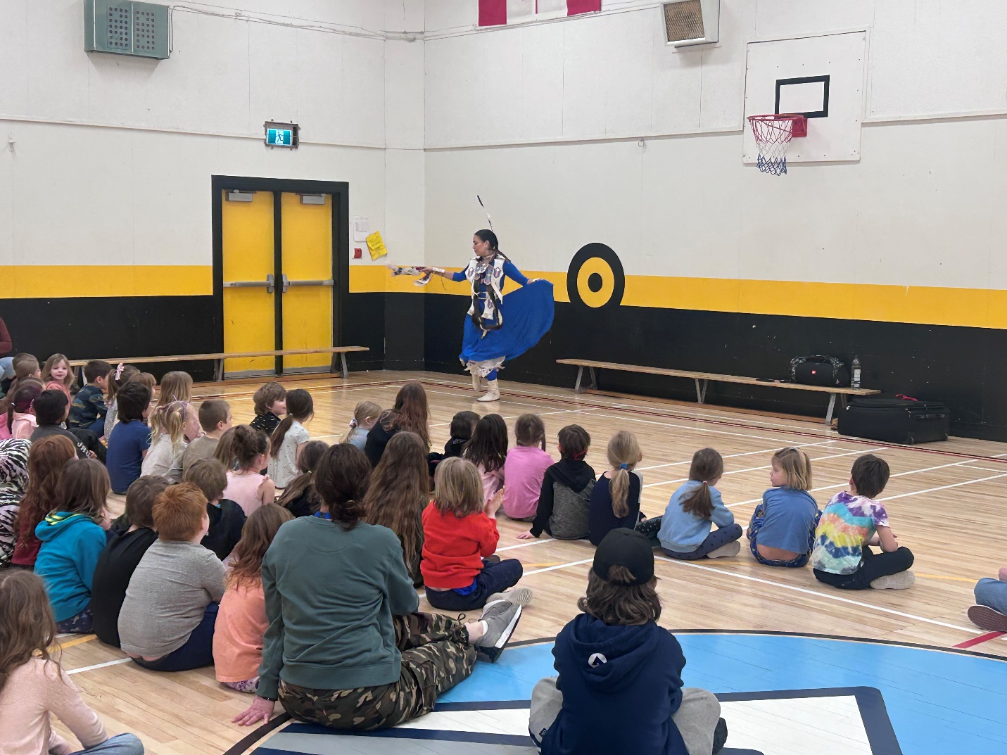 A group of kids sitting on the floor in a gym
Description automatically generated