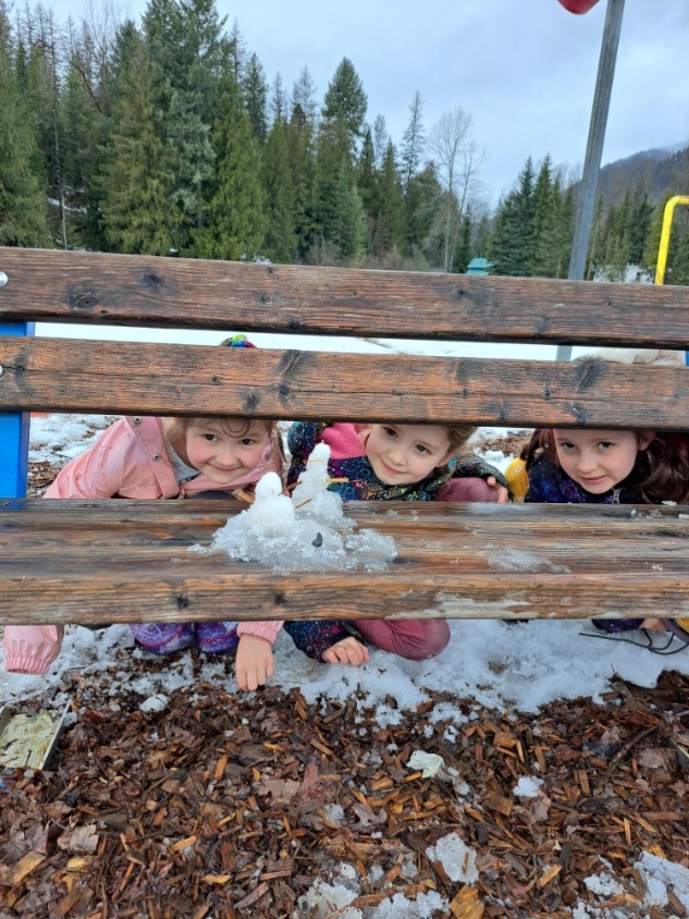 A group of children sitting behind a wooden bench
Description automatically generated