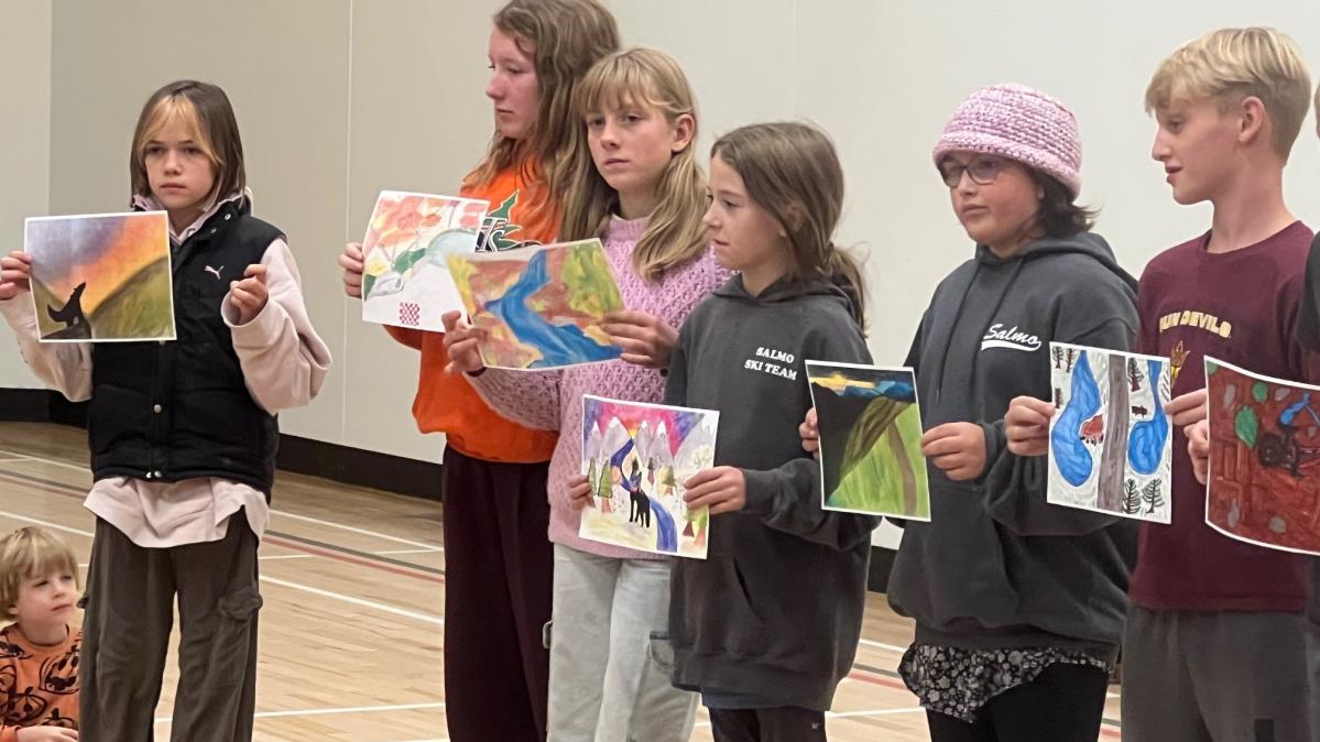 Elementary school students in a gym hold up their artwork for others to see.