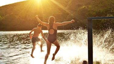 Three children leap off a dock into a lake at sunset