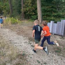 Two young boys run along a gravel trail beside a forest