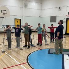 Elementary school students practice taking aim with empty arms in preparation for using an actual archery bow.