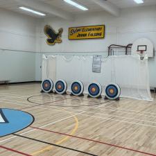 Five archery targets lined up in front of a net at the end of a school gymnasium. 