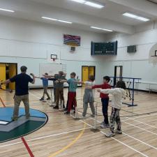 Elementary school students practice taking aim with empty arms in preparation for using an actual archery bow.