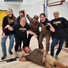 A group of adults wearing matching black jersies pose in mock-ferocious ways.