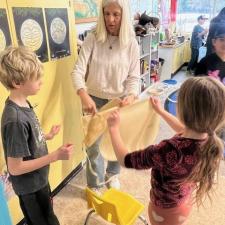 Young students and a teacher holding a hide for a drum