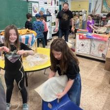 Two young students stretch a hide over the back of a chair