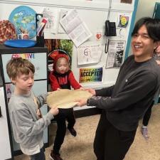 Two young students and a teenager stretch a hide together