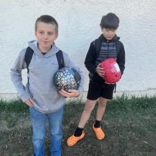 Two boys hold taped up objects in front of a white wall outdoors.