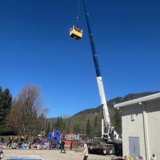 A large white and blue crane holding a yellow cage-bucket with a person in it, and people looking on in front of an elementary school