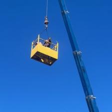 A blue crane holding a yellow bucket high in the sky with a person standing in the bucket
