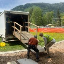 Two men unload a wooden bridge structure from a cargo truck